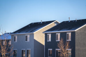 Simple grey American houses viewed from low angle with bare trees and thin layer of frost on the roofs in sunny winter morning